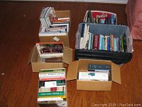 Wide view showing five boxes containing various books arranged on hardwood floor.