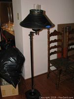 Full view of the 59 inch tall black metal floor lamp with metal shade and base positioned near wooden chairs.