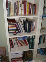 White bookshelf with multiple rows holding a variety of books arranged vertically and horizontally, various height and thickness.
