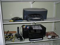 Wide view showing two HP printers and Hallmark Card Studio software box on wire shelving with some cables and accessories.