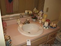 Wide angle photo of bathroom sink area showing bath decor including a stuffed bear, bunny angel, and candles along side a ceramic musical Santa figurine, Sunbeam scale visible.