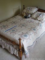 Full view of full-size bed with quilted star-pattern bedspread, pillow shams, and teddy bear on top. Wooden headboard and footboard visible with turned posts.