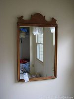 Full front view of the vintage wood framed mirror hanging on a beige wall, showing its rectangular shape and carved top.