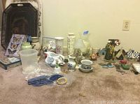 Photo showing two large metal serving trays, several vases, decorative pitchers, small ceramic and glass items, miniature bird house, and various other decor pieces arranged on carpeted floor
