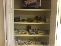 Shelf with various decorative plates including Japanese 5.5 inch plates, vintage Washington DC plates, pasta serving bowls and small baskets arranged on three shelves.