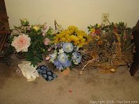 Four faux floral arrangements, gardening gloves, and Vera Bradley eyeglass case shown together on carpet next to a wall outlet