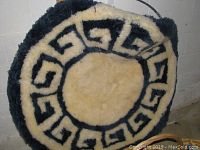 Front view of the 52-inch diameter round sheepskin wall hanging showing the central cream sheepskin and black Greek key pattern around it.