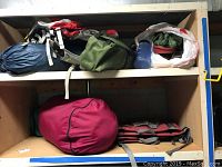 Shelving with rolled tents or sleeping bags in storage bags in various colors, red and gray camp chairs on lower shelf