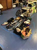 Photo of the overall sports equipment lot showing hockey sticks, helmets, sports balls including soccer, baseball, softball and various clubs.