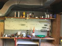 Wide view of workshop bench with hand tools and various hardware items on surface and pegboard above