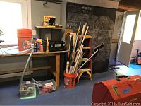 View of basement workspace with buckets, brooms, ladder, toolbag, and red DeWalt container