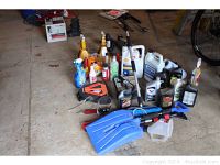 Wide shot of all car maintenance items laid on garage floor including jacks, fluids, brushes, and accessories.