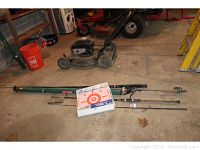 Long view of fishing rods and accessories on concrete floor in garage with other tools in background