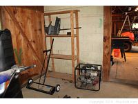 Wide view showing the small boat motor on the top shelf of a wooden shelving unit, the shelving unit structure, and the magnetic shop sweeper on the floor beside it.