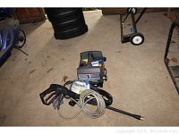 Full view of Ryobi pressure washer unit, spray gun with hose, power cord, and instruction manual on concrete floor.