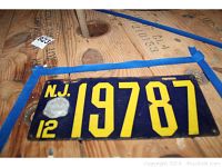 New Jersey dark blue license plate with yellow numbering and rust around edges, placed on wooden surface marked with blue tape