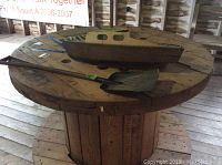 Photo showing the wooden and metal boat model along with the shovel placed on a large wooden spool.