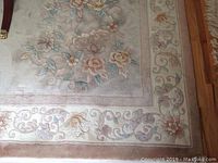 Close-up of one corner of the rug showing floral pastel pattern, pale dusty rose border and pale grey field