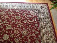 Close-up view of large burgundy and beige rug showing detailed floral pattern and border.