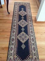 Full view of navy wool runner with beige and rust red geometric pattern on wooden floor.