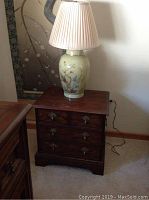 Dark wood nightstand with 3 drawers and brass pull hardware. Lamp on top.