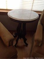 Full view of antique pedestal table with oval marble top, positioned between two chairs, showing table height and shape.