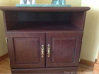 Wooden cabinet-style TV or microwave stand with two doors and an open shelf above, dark wood finish.