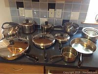Full view of cookware collection arranged on a kitchen counter showing skillets, pots, mixing bowls, kettle, and lids.