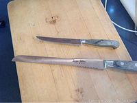 Two serrated Jacques Debarr knives with wooden handles on a wooden surface, different blade lengths