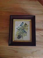 Photo of framed vintage bird print with blue birds perched on branch, wood frame with gold trim.
