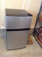 Closed view of a small stainless steel mini refrigerator with separate freezer and fridge doors.