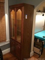 Full view of the wood display cabinet showing the glass doors, wood frame, and overall shape and size.