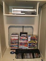 Silver Sony VCR/DVD player on shelf with remote and DVD discs stacked below
