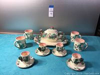 Full tea set displayed on a blue cloth showing teapot on tray, four mugs, and two cups with saucers