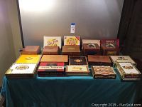 Photo showing arranged assortment of 15 cigar boxes on a blue cloth, highlighting variety in sizes, colors, and branding.