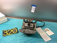 Front view of the Polaroid Automatic 320 Land Camera with open front panel, instruction manuals, and part of carrying case.