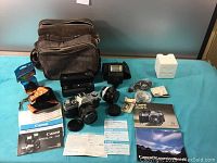 Overview of Canon AE-1 camera kit laid out on blue cloth including camera, lenses, flash, manuals, straps, and accessories.