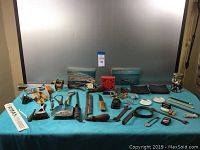 Wide view of all items in the lot laid out on a table, showing multiple old metal hand tools, ratchets, a red tool, some miscellaneous metal items, and the jar of buttons.