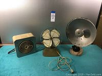 Three vintage electric appliances: small heater, fan, and large heater with conical reflector.