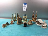 Nine village miniature buildings including churches, cottages, and clock tower on blue fabric surface