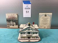 Rockwell's Studio miniature model with deed of ownership and booklet in background on blue cloth against gray wall.