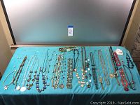 Wide view of the assortment of costume jewelry necklaces and sets on a turquoise cloth, showing a variety of styles and colors including beaded strands, pendants, and chain necklaces.