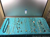 Multiple assorted costume jewelry necklaces displayed on a blue cloth background, showing variety in bead sizes, chains, and pendants.