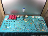 Overview of spread costume jewelry on blue cloth, showing earrings, rings, and other small jewelry pieces.