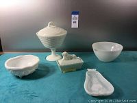 Five vintage milk glass and white glass serving pieces displayed on a teal surface showing their shapes and styles.