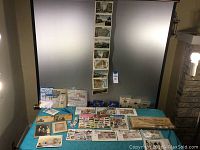 Overview of the lot showing postcards, newspapers, and stamp books spread on table.