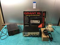 Photo showing all items on a table including the Uniden Grant XL CB radio with box, Afterburner linear amplifier, MFJ tuner, microphone with cable in box, and the antenna.