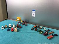 Overview of all vintage Matchbox cars and other toy vehicles along with bear and tricycle on blue cloth.