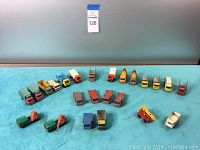 Front view of 26 vintage Matchbox trucks including various types like dump, flatbed, and mixer trucks arranged on blue surface.