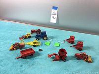 Overview of vintage toy farm equipment spread on blue surface showing various farm vehicles and implements in red, yellow, and blue colors.